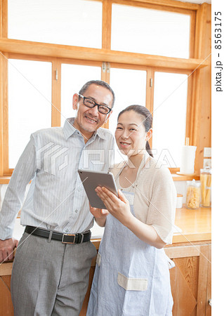 タブレットPCをキッチンで見る熟年夫婦 8563175