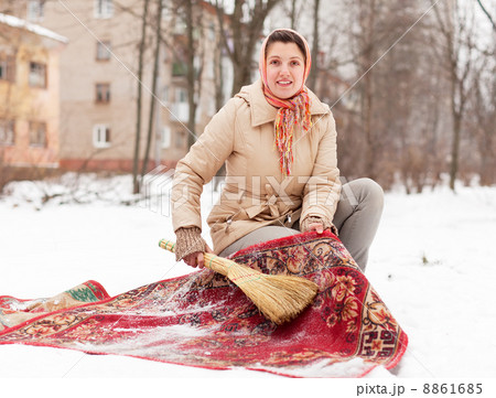 Young woman cleans red rug with snow 8861685