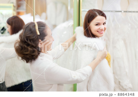woman with girl chooses white fur cape at shop 8864348