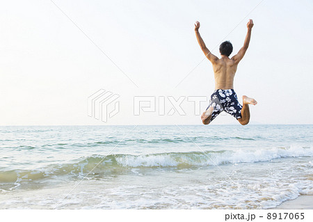 海でジャンプする男性の後ろ姿の写真素材
