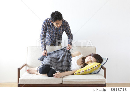 ソファで眠る女性にタオルケットをかける男性の写真素材
