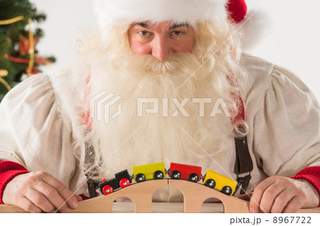 Santa Claus sitting and playing with railway toy at home 8967722