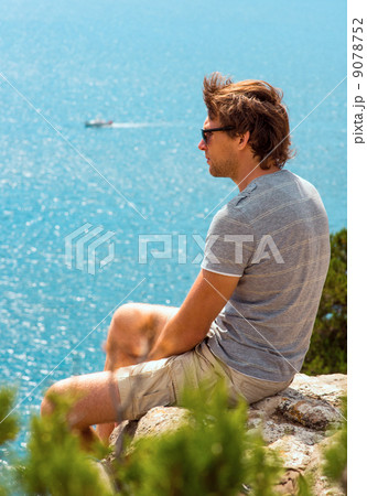 Young Man relaxing Outdoor on rocky cliff sitting and looking on Sea Summer time Traveling Lifestyle 9078752