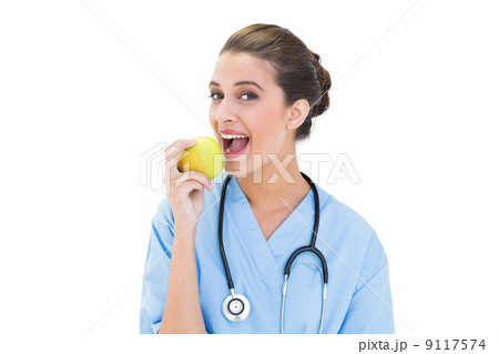 Delighted brown haired nurse in blue scrubs eating a green apple Delighted brown haired nurse in blue scrubs eating a green apple 9117574