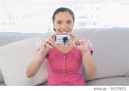 Smiling woman sitting on sofa taking a picture Smiling woman sitting on sofa taking a picture 9117623