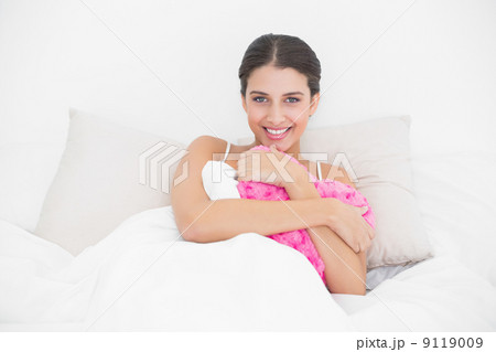 Happy young brown haired model in white pajamas hugging a heart 9119009