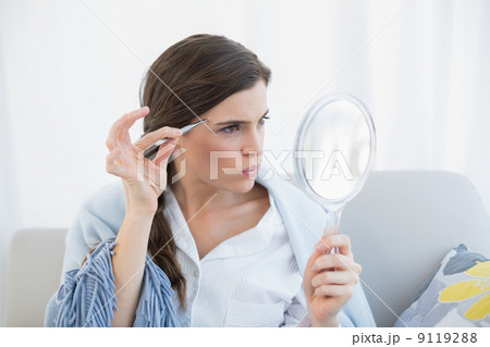 Focused casual brown haired woman in white pajamas plucking her 9119288