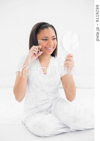Smiling young dark haired model using eyelash curler 9119299