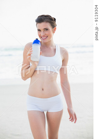 Joyful slim brown haired model in white sportswear holding a bot Joyful slim brown haired model in white sportswear holding a bot 9119304