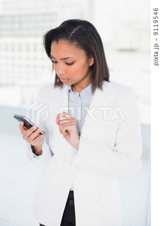 Thinking young dark haired businesswoman looking at her mobile p Thinking young dark haired businesswoman looking at her mobile p 9119546