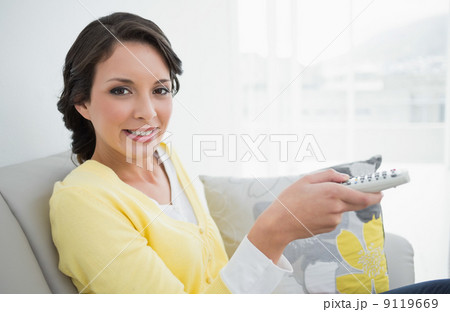 Pleased casual brunette in yellow cardigan changing tv channel Pleased casual brunette in yellow cardigan changing tv channel 9119669