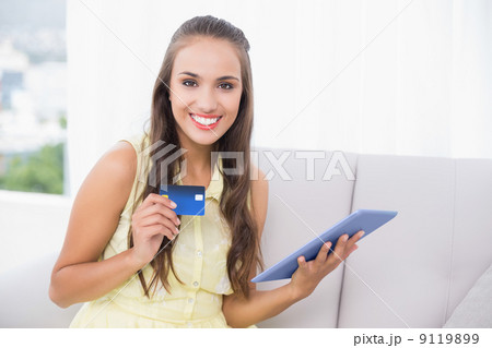 Smiling young brunette holding credit card and tablet Smiling young brunette holding credit card and tablet 9119899