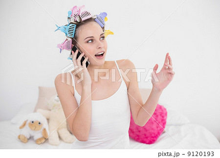 Surprised natural brown haired woman in hair curlers making a ph 9120193