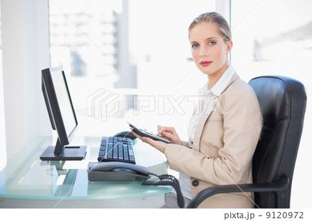 Side view of blonde businesswoman using calculator 9120972