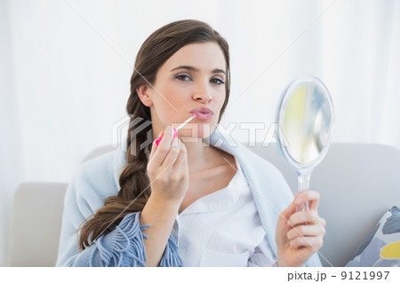 Pouting casual brown haired woman in white pajamas applying glos Pouting casual brown haired woman in white pajamas applying glos 9121997