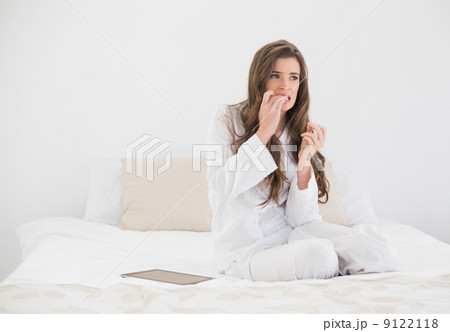 Worried casual brown haired woman in white pajamas sitting on he Worried casual brown haired woman in white pajamas sitting on he 9122118