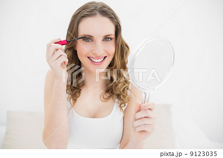 Young woman using mascara while holding a mirror 9123035