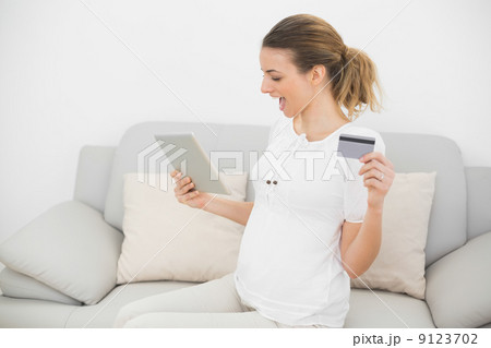 Cute cheering pregnant woman using her tablet for home shopping Cute cheering pregnant woman using her tablet for home shopping 9123702