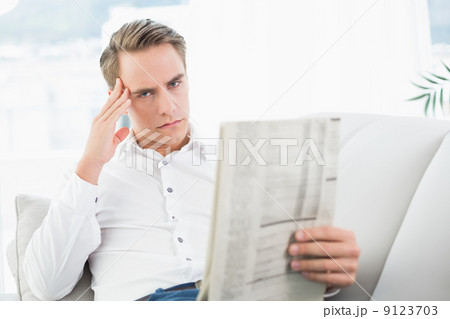 Portrait of a serious relaxed man reading newspaper on sofa 9123703