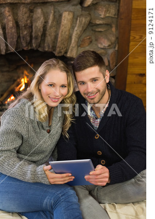 Lovely couple using tablet PC in front of lit fireplace Lovely couple using tablet PC in front of lit fireplace 9124171