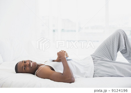 Smiling Afro man resting with digital tablet in bed 9124196