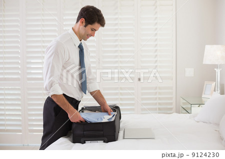 Smiling businessman unpacking luggage at a hotel bedroom Smiling businessman unpacking luggage at a hotel bedroom 9124230