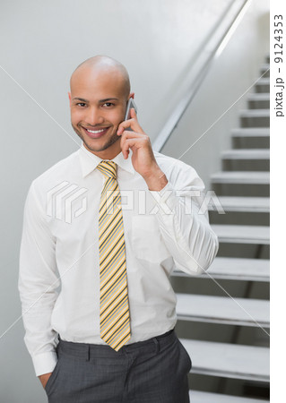 Smiling businessman using cellphone against staircase Smiling businessman using cellphone against staircase 9124353