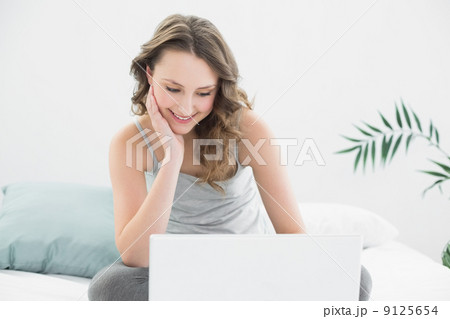 Smiling casual brunette looking at laptop in bed Smiling casual brunette looking at laptop in bed 9125654