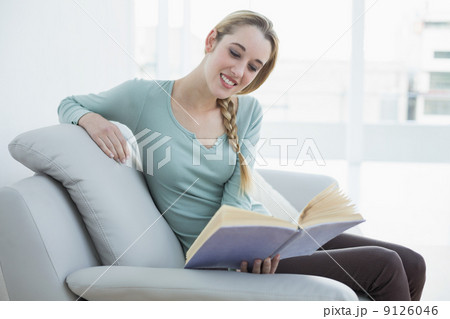 Young casual woman reading a book while sitting smiling on couch Young casual woman reading a book while sitting smiling on couch 9126046