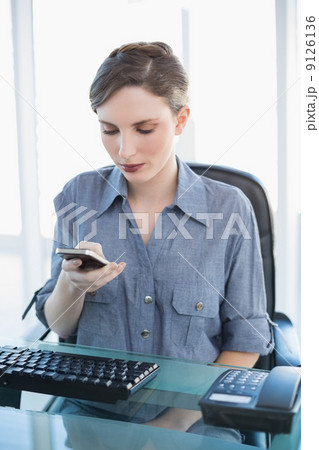 Young businesswoman using her smartphone sitting at her desk Young businesswoman using her smartphone sitting at her desk 9126136