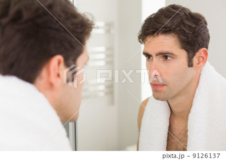 Serious young man looking at self in bathroom mirror Serious young man looking at self in bathroom mirror 9126137