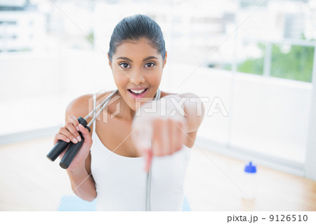 Excited toned brunette sitting on floor with skipping rope Excited toned brunette sitting on floor with skipping rope 9126510