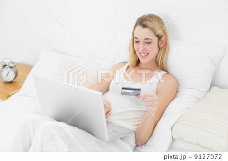 Gorgeous woman home shopping with her notebook lying on her bed 9127072