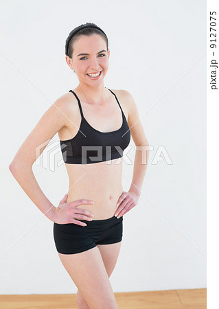 Smiling toned woman with hands on hips in fitness studio Smiling toned woman with hands on hips in fitness studio 9127075