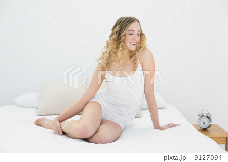 Pretty smiling blonde sitting on bed relaxing Pretty smiling blonde sitting on bed relaxing 9127094