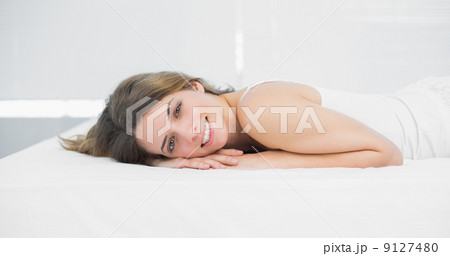 Attractive brunette woman smiling cheerfully at camera lying on 9127480
