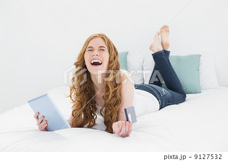 Happy blond with tablet PC and credit card in bed 9127532