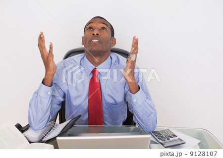 Serious Afro businessman looking up at desk Serious Afro businessman looking up at desk 9128107