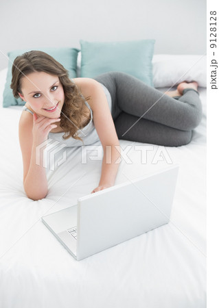 Smiling casual young brunette with laptop in bed 9128128