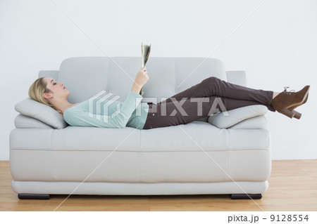 Attractive blonde woman reading newspaper lying on couch 9128554