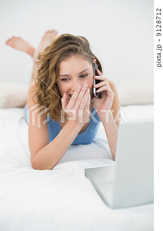 Beautiful young woman lying on her bed phoning with her smartpho Beautiful young woman lying on her bed phoning with her smartpho 9128712