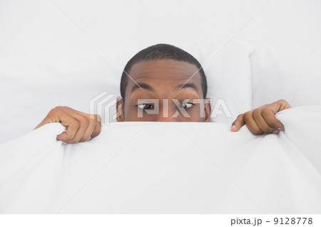 Shocked Afro man covering face with sheet in bed Shocked Afro man covering face with sheet in bed 9128778