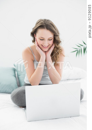 Smiling casual brunette looking at laptop in bed 9129085