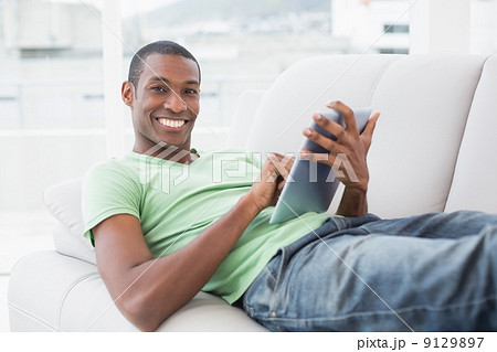 Casual smiling Afro man using digital tablet on sofa Casual smiling Afro man using digital tablet on sofa 9129897