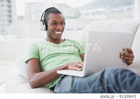 Smiling Afro man with headphones using laptop on sofa 9130641