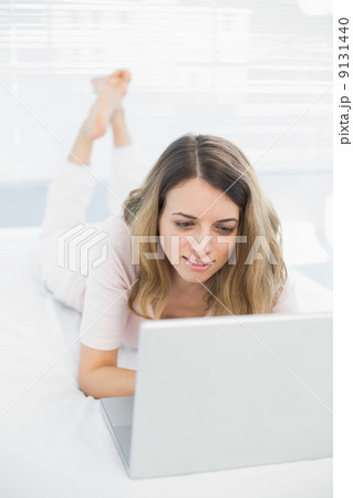 Cute young woman using her notebook lying on her bed Cute young woman using her notebook lying on her bed 9131440