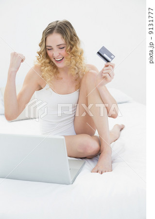 Pretty excited blonde sitting on bed using laptop and credit car Pretty excited blonde sitting on bed using laptop and credit car 9131777