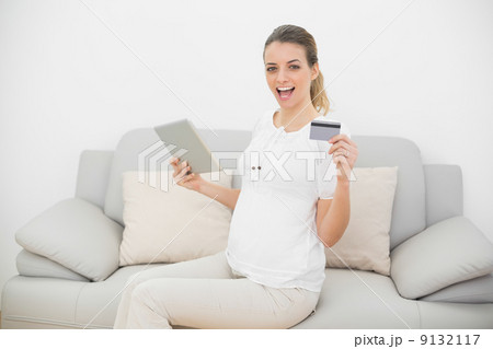 Cheering pregnant woman showing her tablet and credit card looki 9132117