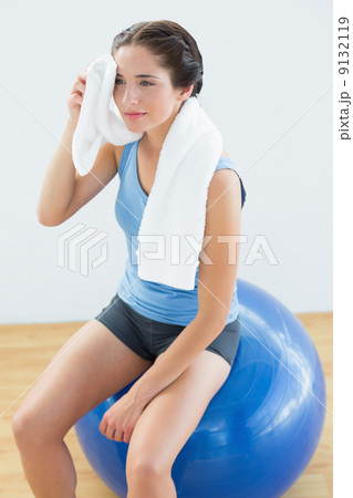 Tired woman with towel around neck on exercise ball 9132119