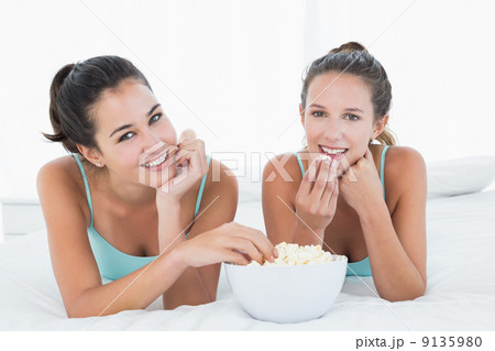 Smiling female friends eating popcorn in bed 9135980